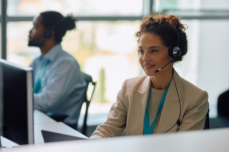 A female office worker wearing headphones, smiling while looking at computer