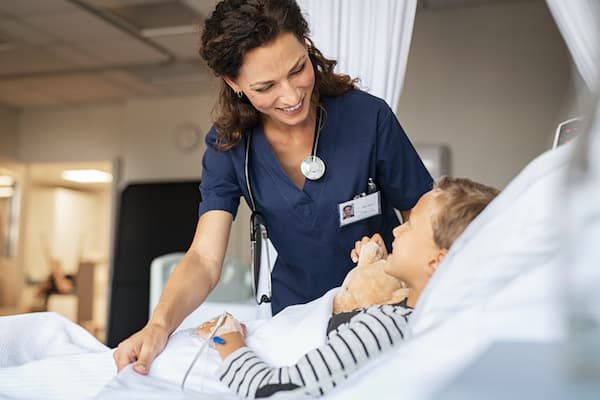 A smiling nurse tucking a young patient's bed