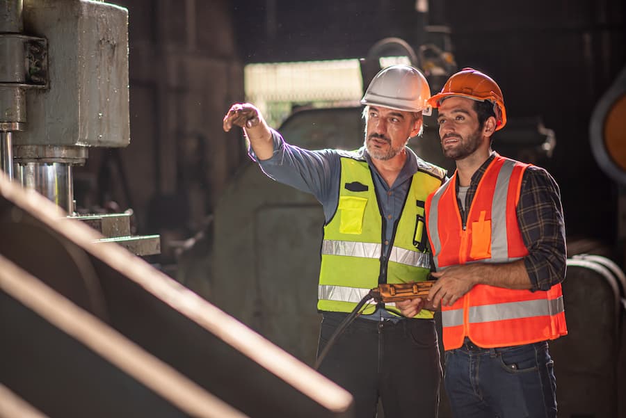 Supervisor speaking with a worker beside machinery,